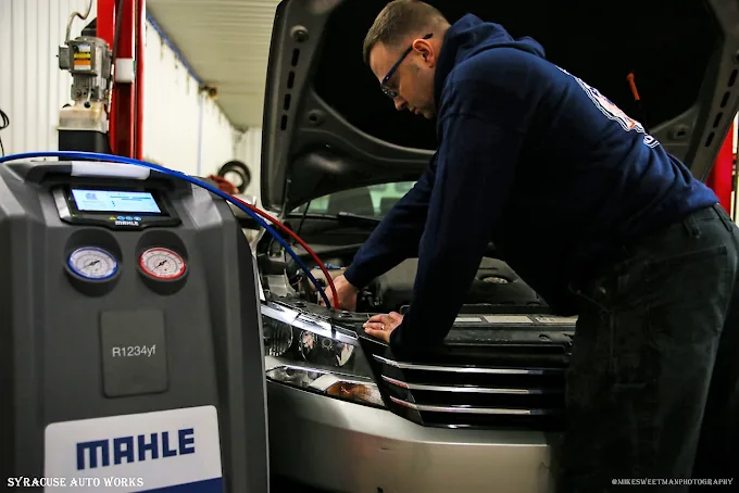 Technician connecting an R-1234yf air-conditioning recovery machine to a car in the shop.